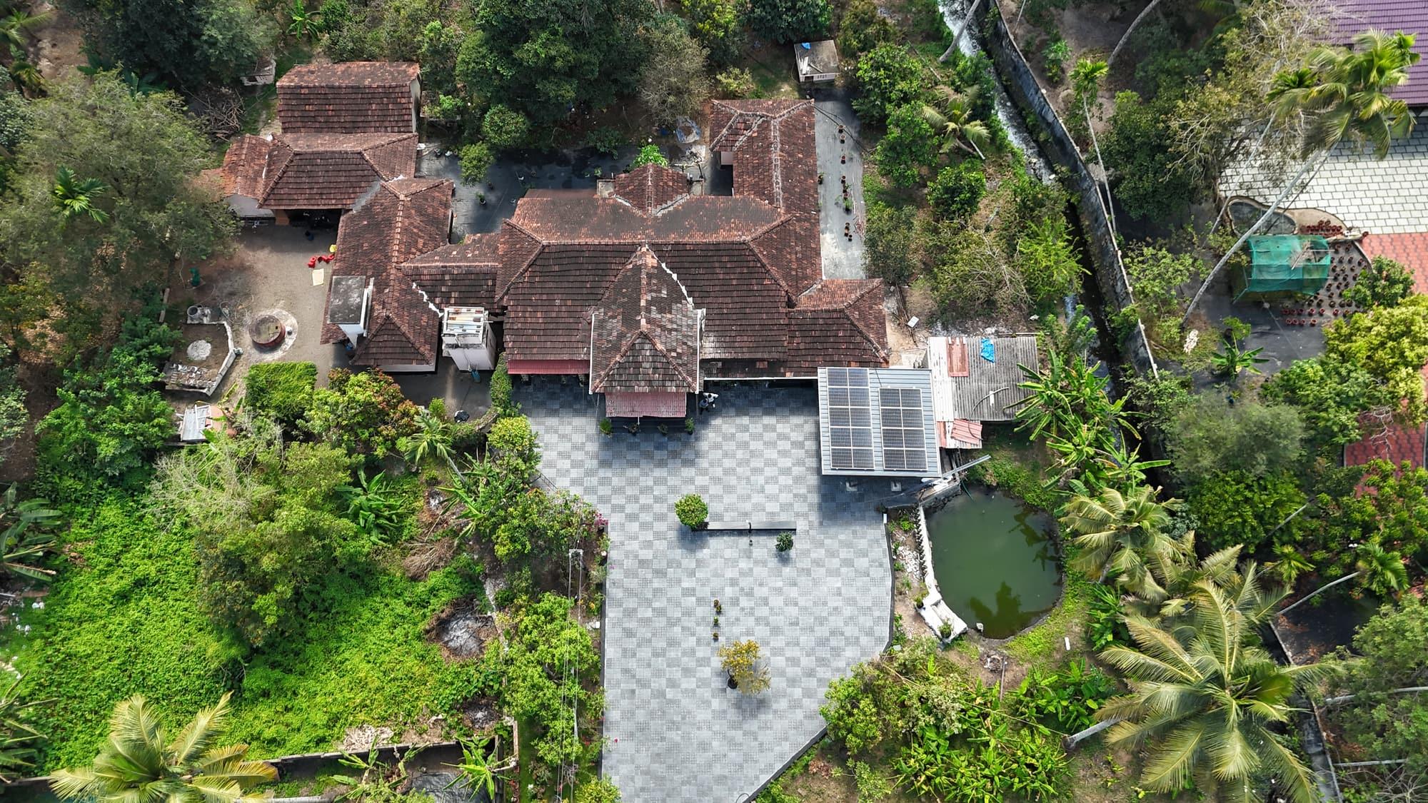 Aerial view of a traditional Kerala home among coconut palms, with a SEDNA rooftop solar array beside the courtyard